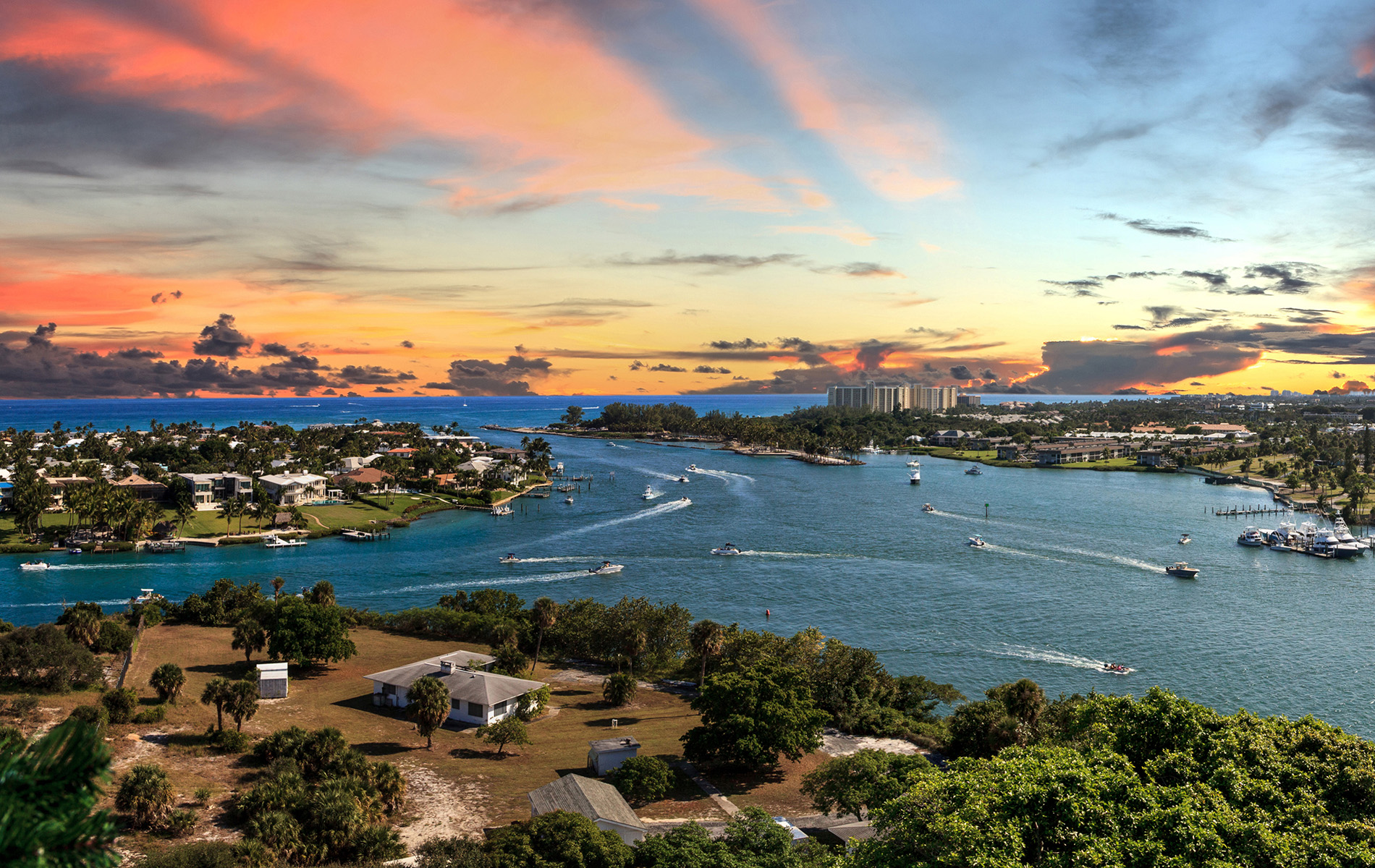 The image shows a scenic view of a coastal city with a vibrant sunset, boats on the water, and a skyline with buildings.