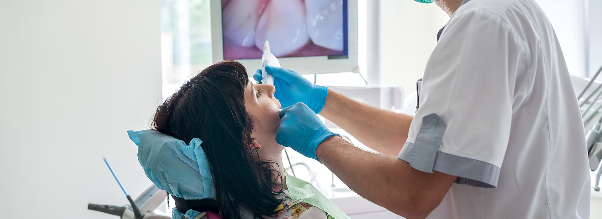 In the image, a dental professional is performing a procedure on a patient in a dental office. The professional is using specialized equipment and wearing protective gloves.