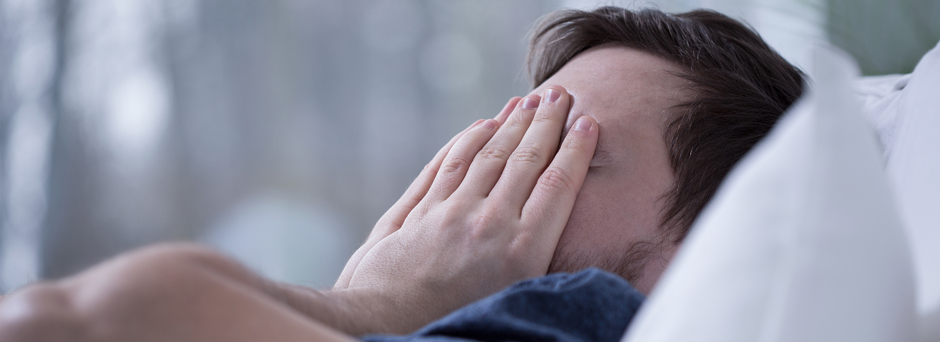 A person lying in bed with a hand covering their face, appearing to be in a state of sadness or distress.