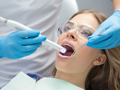 The image shows a dental professional performing an oral examination on a patient, using a digital device to capture the process.