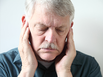 The image shows a man with his hand on his ear, appearing to be in pain or discomfort.